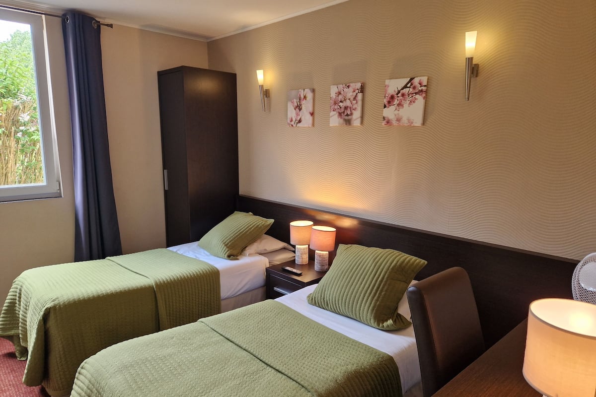 A hotel room with two beds, a nightstand, a lamp, and wall-mounted artwork.