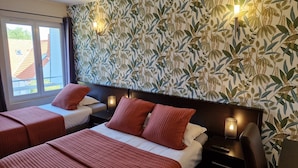 Une chambre d’hôtel avec deux lits, une grande fenêtre et un mur orné d’un motif végétal.