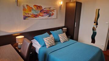 A hotel room with a large bed, a desk, a chair, a lamp, and a wall-mounted artwork.