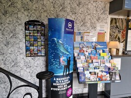 Uma área de recepção de hotel com um grande cartaz de baleia, uma exposição de postais e uma placa indicando um restaurante.