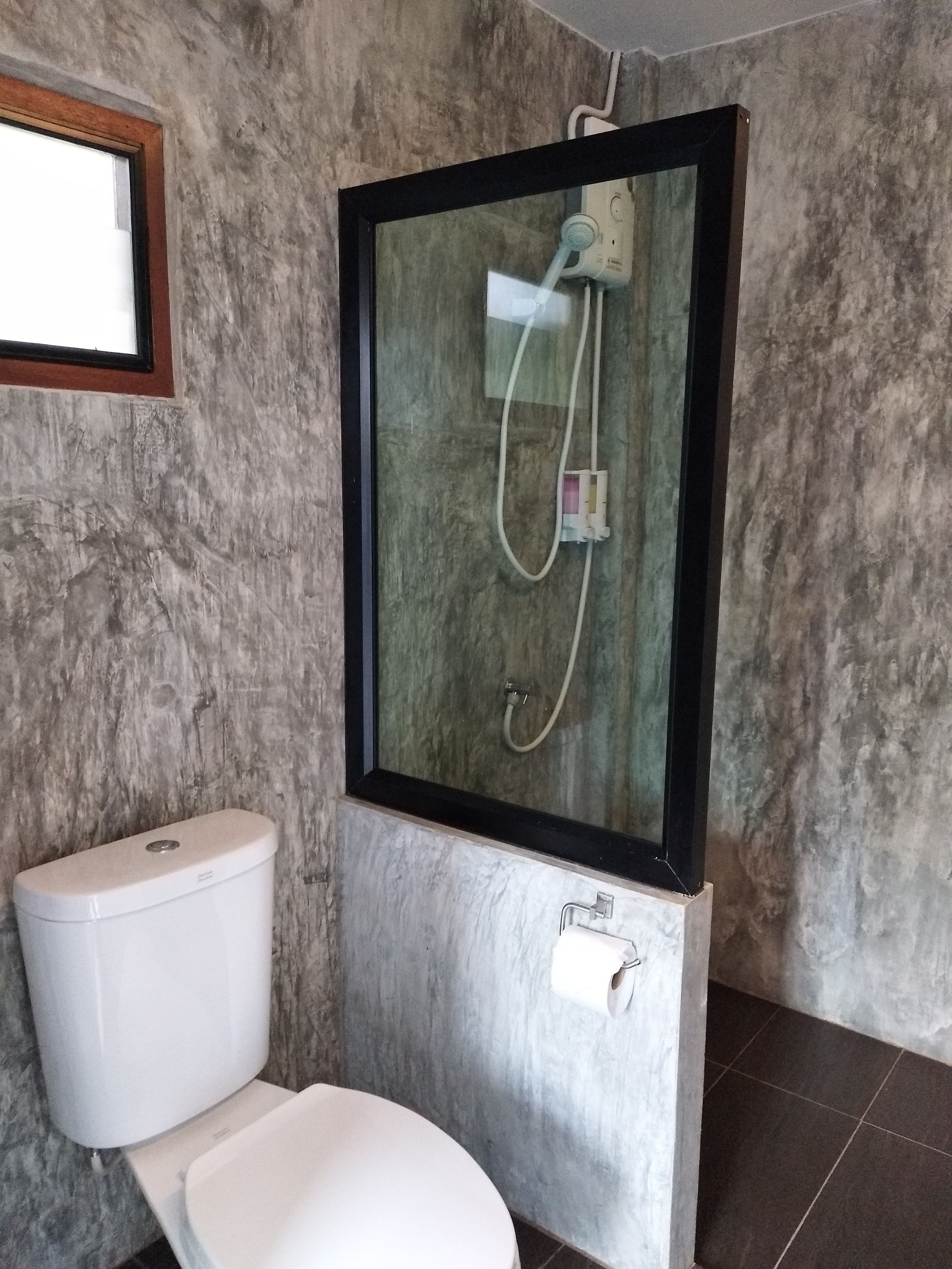 A bathroom with a toilet, a shower with a glass enclosure, and a marble wall.