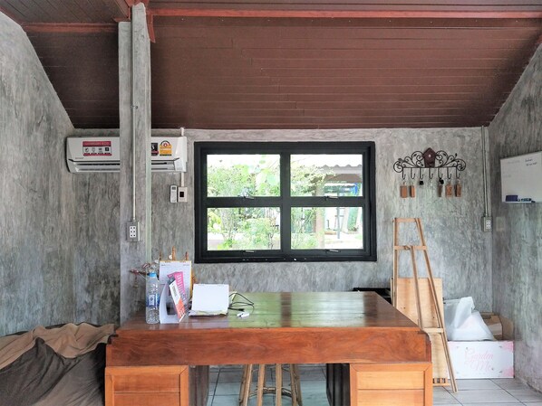 Una habitación con una mesa de madera, una ventana que da a zonas verdes, una pizarra y un equipo de aire acondicionado instalado en la pared.