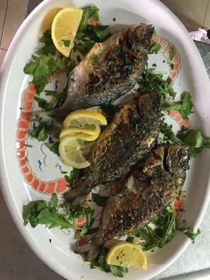 A plate with grilled fish and lemon slices, garnished with greens. - Cinquestelle-albergo del centro storico (Centola)
