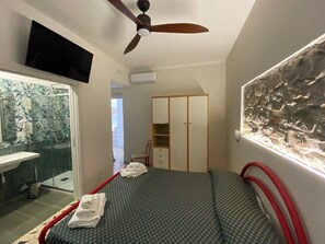 A bedroom with a bed, a ceiling fan, a wardrobe, and a shower area. - Cinquestelle-albergo del centro storico (Centola)