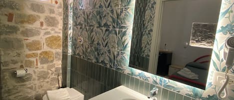 A bathroom with a stone wall, a white sink, a bidet, and a mirror with floral tile backsplash.