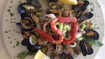 Una bandeja de mariscos con mejillones, almejas, camarones y rodajas de limón sobre un plato blanco.