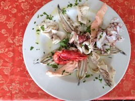 Un plato de mariscos, con pulpo, camarones y pescado, adornado con hierbas, sobre un plato blanco.