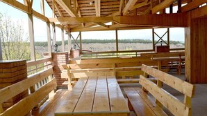 An outdoor wooden pavilion with benches and picnic tables, large windows, and a brick fireplace.