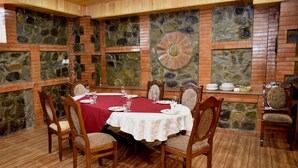 A dining area with a round table set for six, surrounded by wooden chairs with cushioned seats. The walls are adorned with stone panels and a decorative sunburst design.