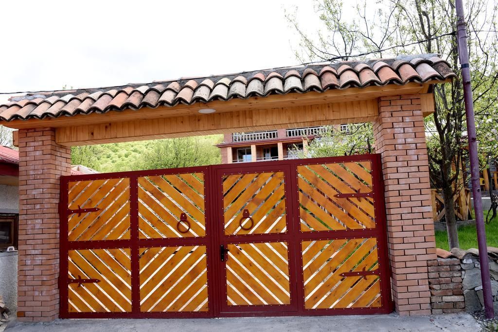 Una entrada con reja, estructura de madera y ladrillo, techo de tejas y vista de un edificio al fondo.