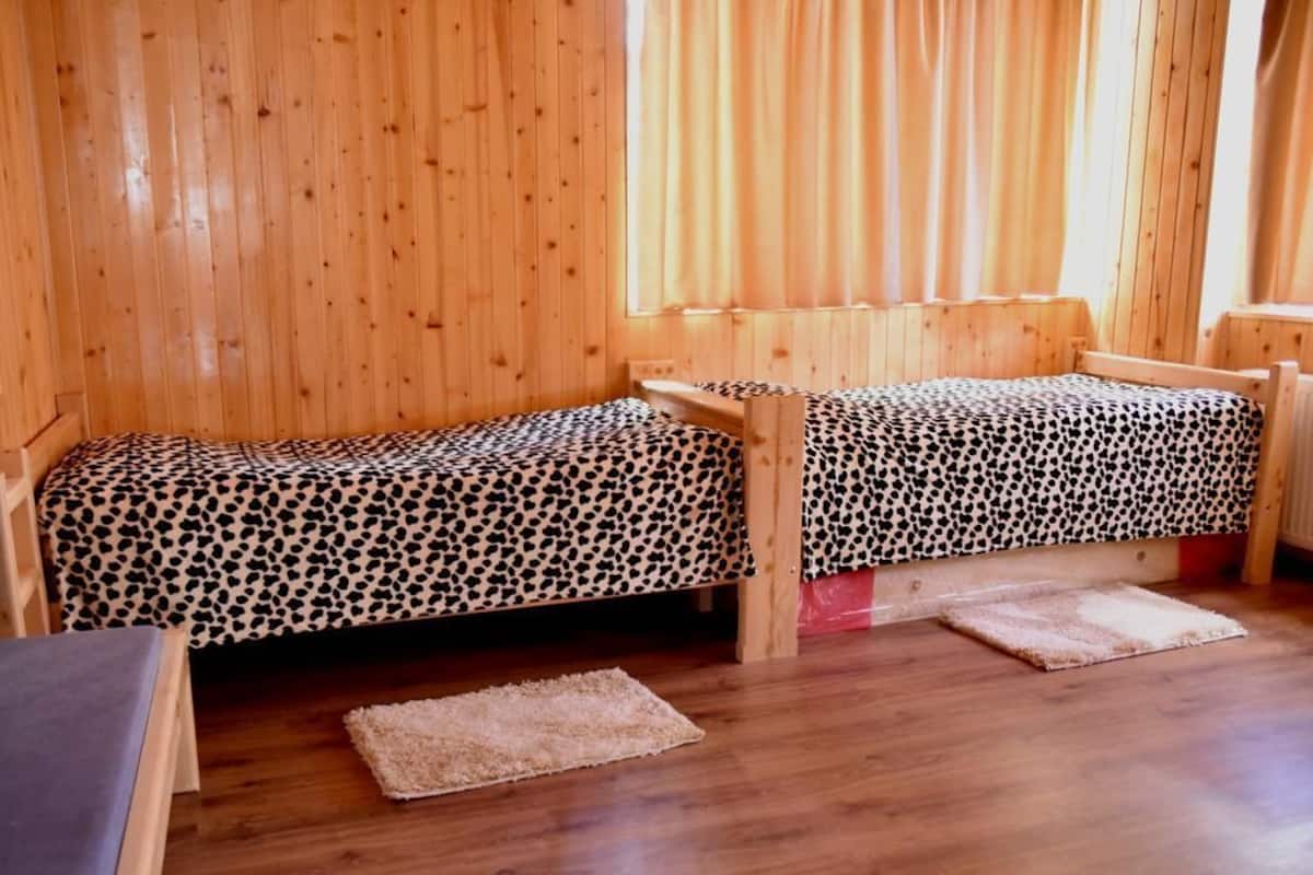 A wooden cabin with two single beds, each with a leopard print bedspread, and a small table between them.