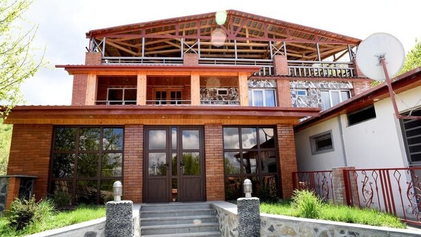 A two-story house with a wooden balcony, stone steps, and a satellite dish.