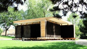 Een gebouw met een houten gevel en een plat dak, omringd door bomen en gras.