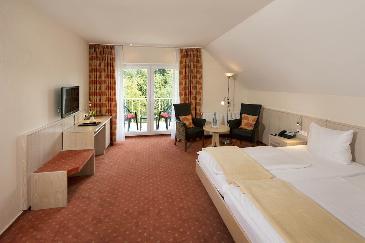 Een hotelkamer met een bed, bureau, stoel, televisie en een balkon met stoelen.