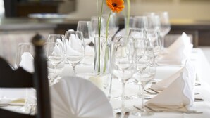 Een eettafel gedekt met verschillende wijnglazen, witte servetten en een vaas met één oranje bloem.