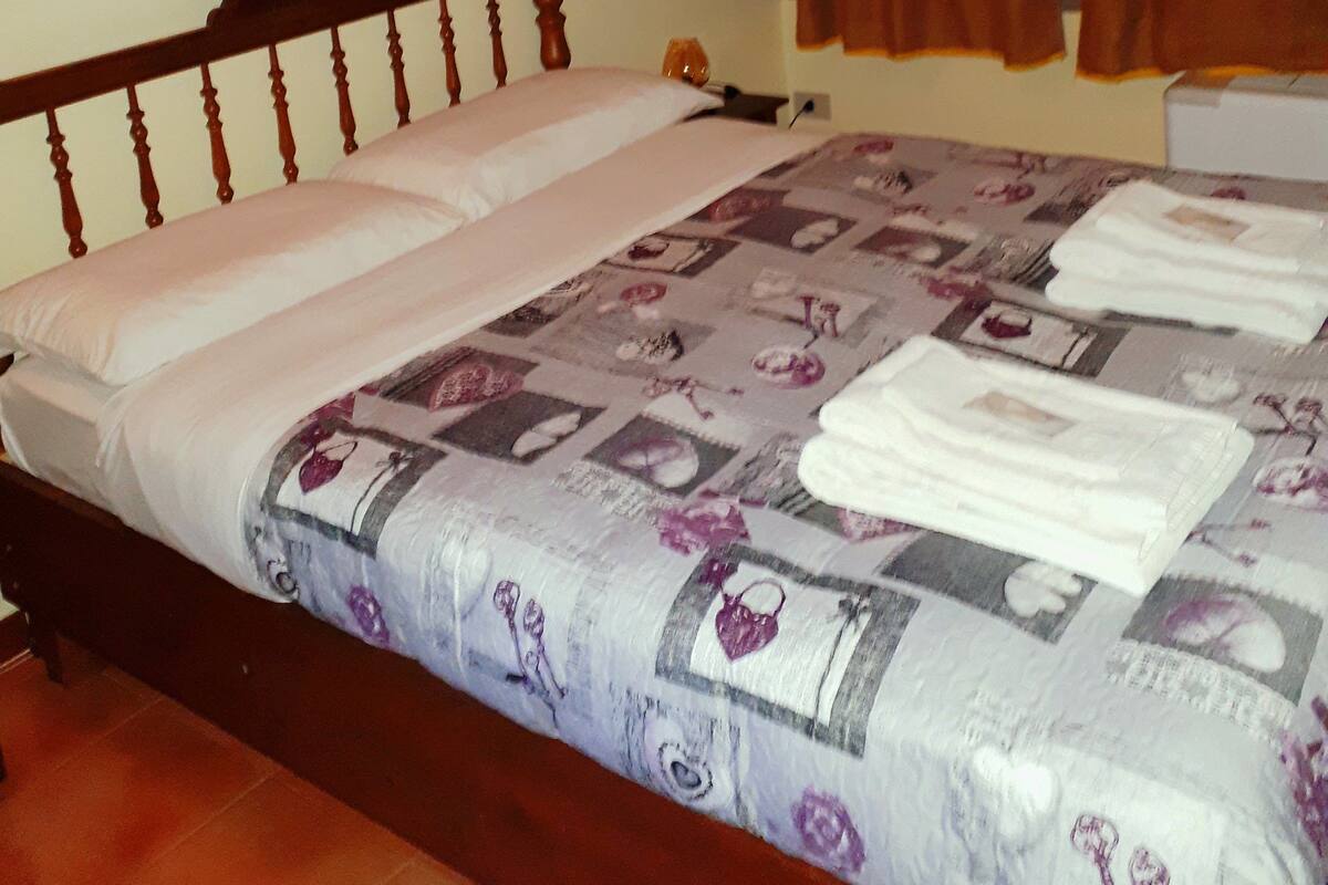 Une chambre à coucher avec un lit en bois, une couvre-lit à motifs floraux, un tableau représentant une maison et des rideaux marron.