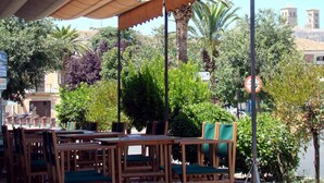 An outdoor seating area with wooden tables and chairs, surrounded by lush greenery and palm trees. - Hostal - Restaurante Emilia (Trujillo)