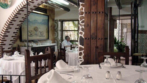 A restaurant with tables set for dining, a painting on the wall, and a stone pillar. - Hostal - Restaurante Emilia (Trujillo)