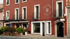 A red building with white trim, labeled "Hostal Emilia." It features multiple windows, some with balconies, and a sign for "El Obrador Pasta." - Hostal - Restaurante Emilia (Trujillo)