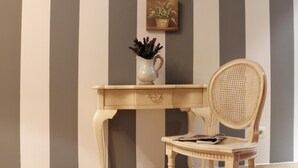 A room with a striped wall, a wooden desk with a vase, and a wicker chair. - Hostal - Restaurante Emilia (Trujillo)