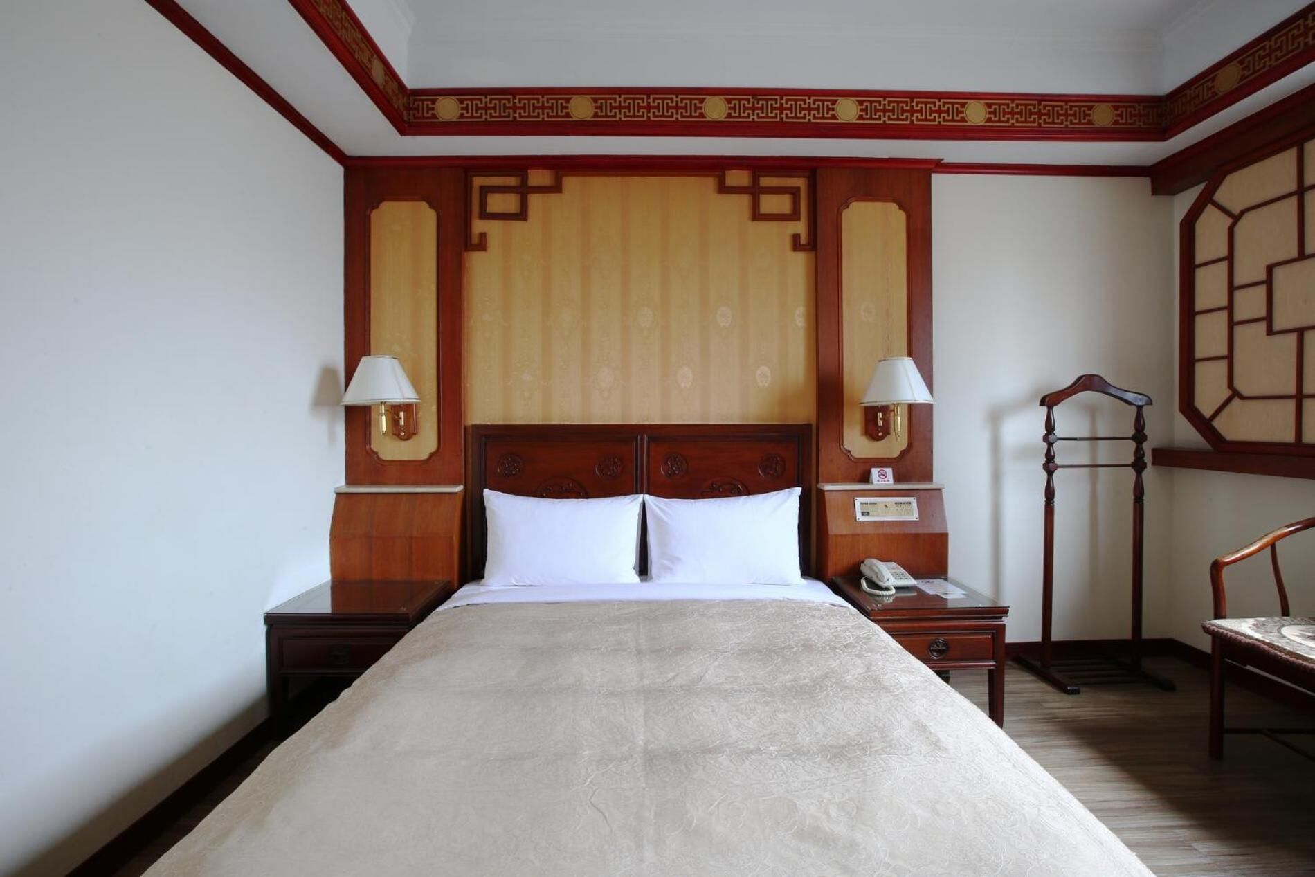 Une chambre d’hôtel avec un grand lit, deux tables de chevet, une petite table, un bureau, une chaise et une armoire.