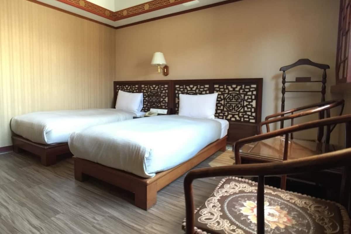 A hotel room with two beds, a wooden headboard, a nightstand, a lamp, and a wooden chair.