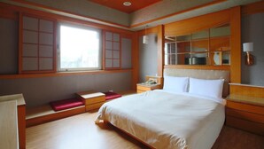 A traditional Japanese-style bedroom with a large bed, wooden paneling, sliding doors, and a small bedside table with a lamp. - Hua Du Hotel (Keelung)