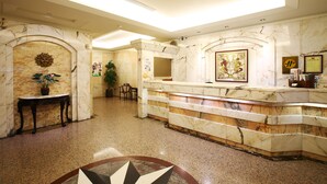 A lobby with marble reception desk, a sun motif on the wall, and a framed artwork. - Hua Du Hotel (Keelung)