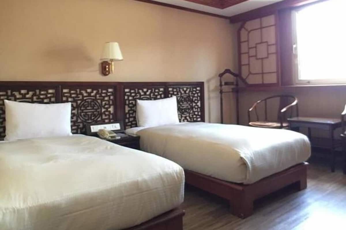 A hotel room with two beds, a desk, a chair, and a window.
