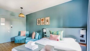 Une chambre d’hôtel avec un lit, un canapé et un bureau. Il y a des serviettes sur le lit et une lampe sur le bureau.
