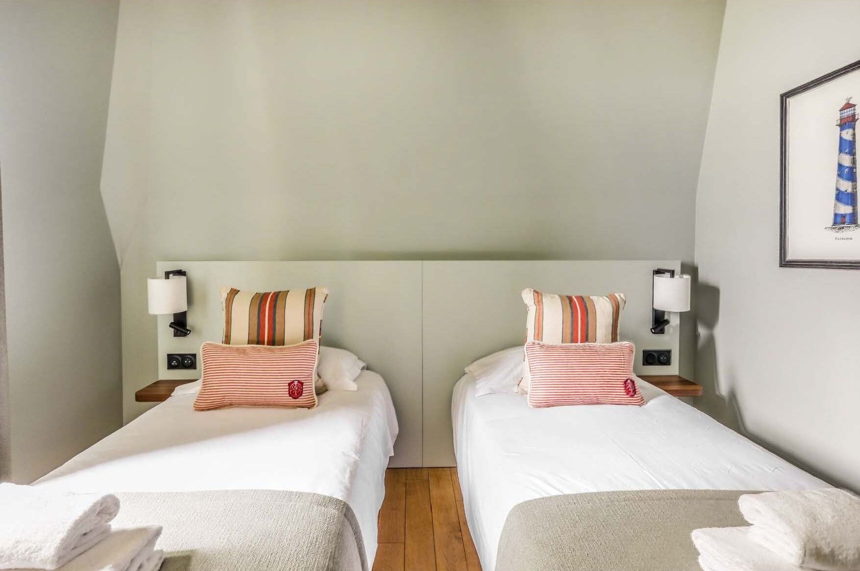 Habitación doble con dos camas, cada una con almohadas a rayas y una mesita de noche con lámpara.