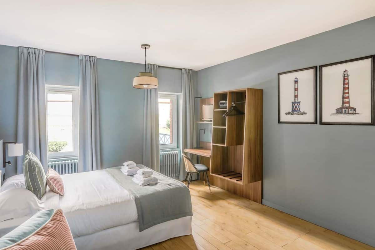 Een slaapkamer met een bed, een bureau, een stoel, een kledingkast en twee ingelijste foto's aan de muur.