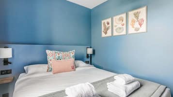 A hotel room with a blue wall, a bed with white bedding, two pillows, a bedside table with a lamp, and three framed pictures on the wall.