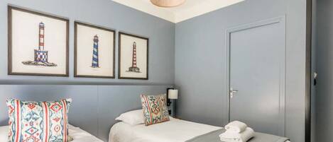 Habitación de hotel con dos camas, una puerta y tres cuadros con imágenes de faros en la pared.