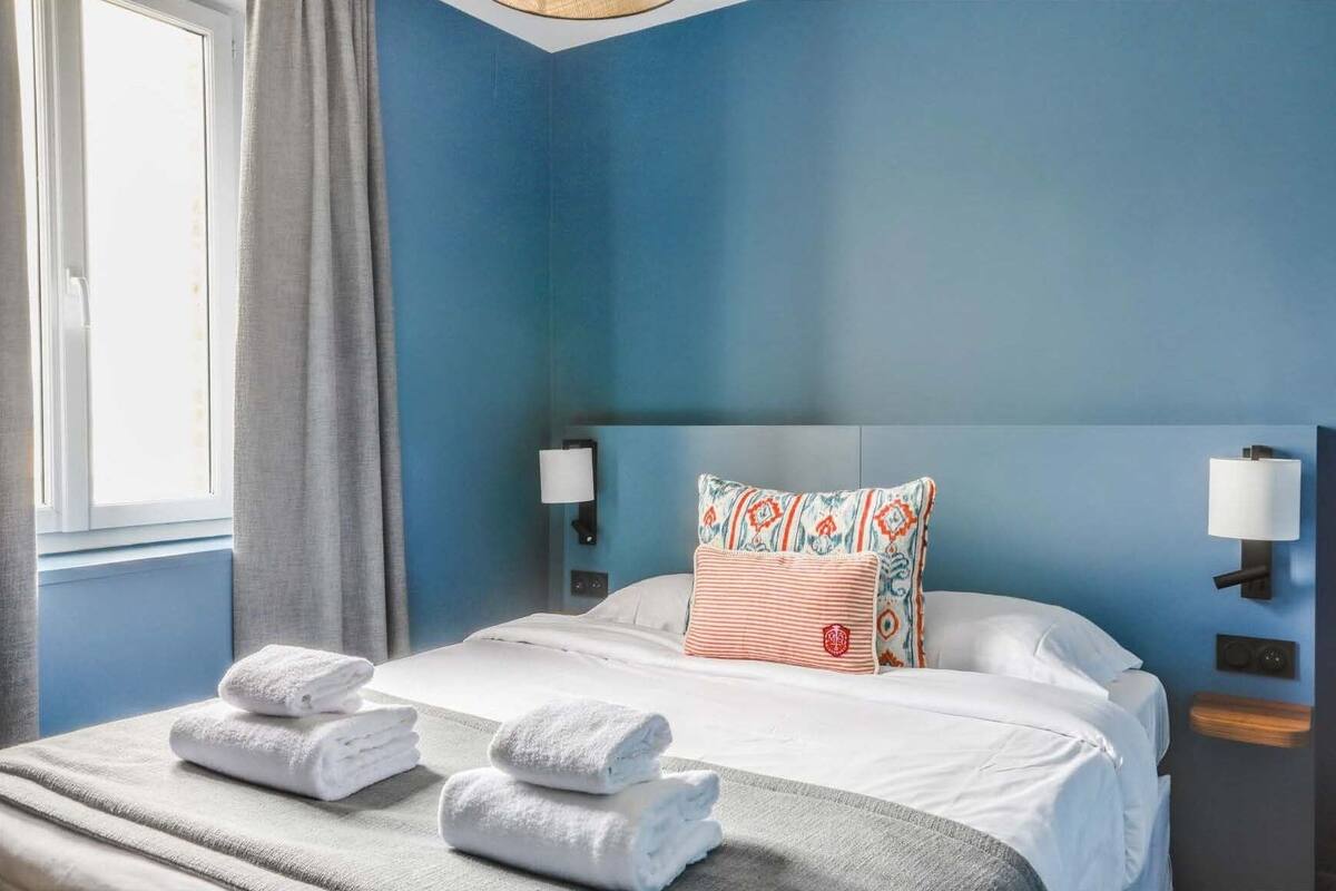 Een hotelkamer met een groot bed, twee kussens, een nachtkastje en een raam met gordijnen.