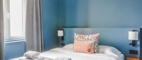 A hotel room with a large bed, two pillows, a nightstand, and a window with curtains.
