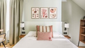 Une chambre d’hôtel comprenant un lit, deux tables de chevet, une chaise et un mur orné de trois tableaux encadrés.