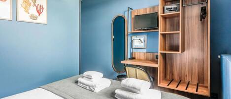 Una habitación de hotel con cama, escritorio con televisor, espejo y armario.