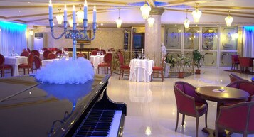 Un amplio comedor con piano, candelabros y sillas rojas.