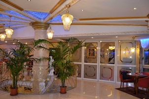 Un hall de lujo con columnas ornamentadas, grandes plantas en macetas y elegantes lámparas de araña.