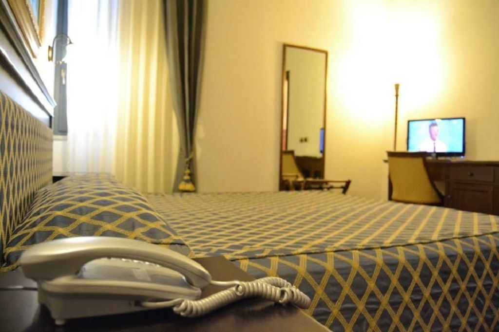 Una habitación de hotel con cama, teléfono en la mesita de noche, televisor, espejo y cómoda.