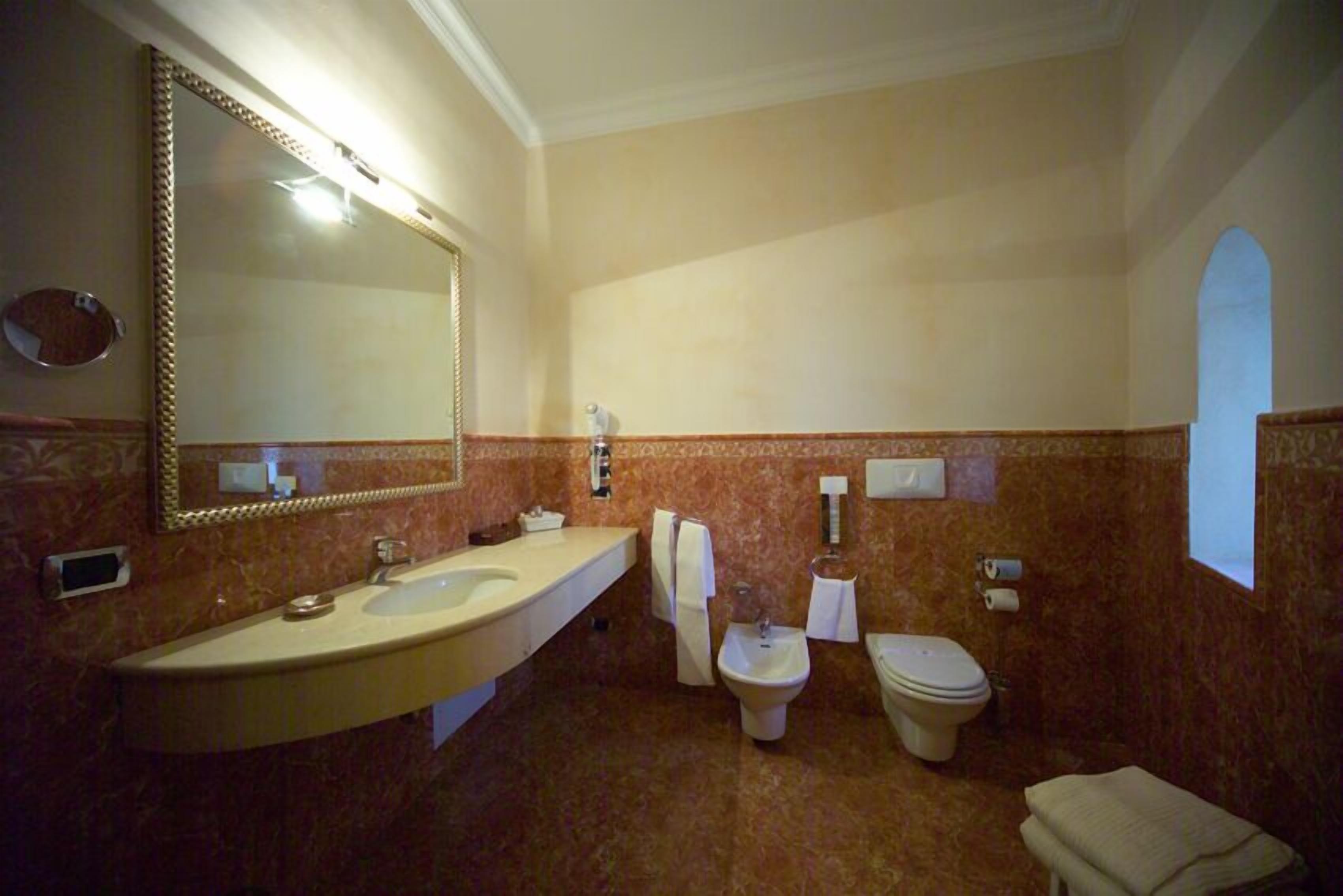 Ein Badezimmer mit einem großen Spiegel, zwei Waschbecken, einem Bidet und einer Toilette.
