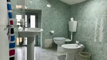 Un bagno con lavandino, WC, bidet e porta carta igienica a parete.