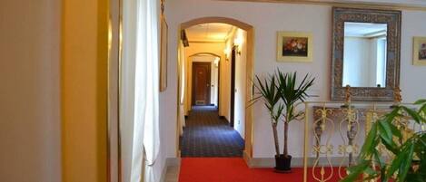 A hotel hallway with a red carpet, a potted plant, and a decorative mirror.