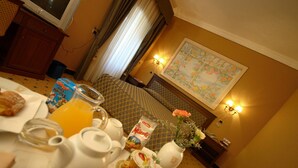 A hotel room with a dining table set for breakfast, a bed with a floral wall hanging, and a television in the corner. - Hotel Don Carlo 4S (San Marco Argentano)