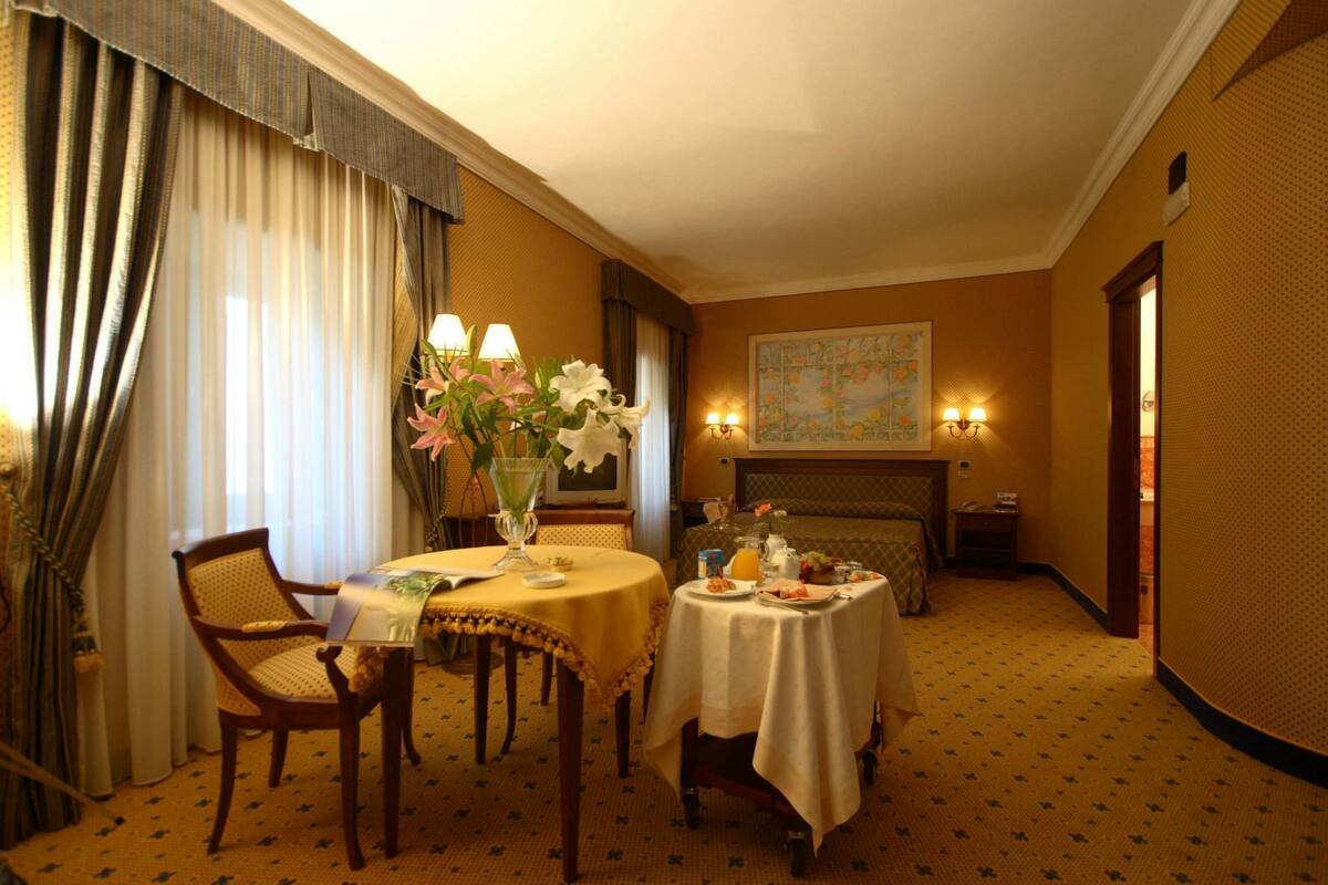 Ein Hotelzimmer mit Esstisch für zwei Personen, einer Blumenvase, einem Kamin und einer Karte an der Wand.