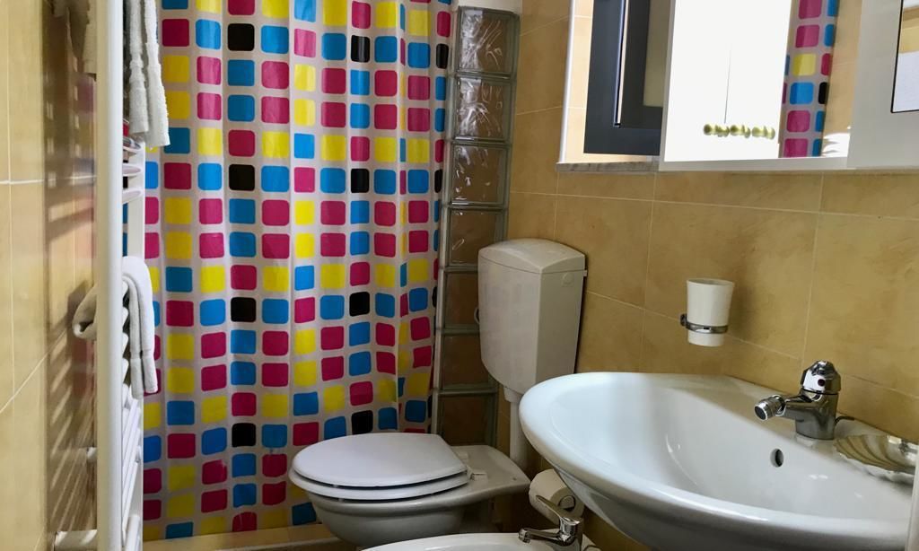 Un baño con inodoro, lavamanos y cortina de ducha con un estampado cuadrado de colores.