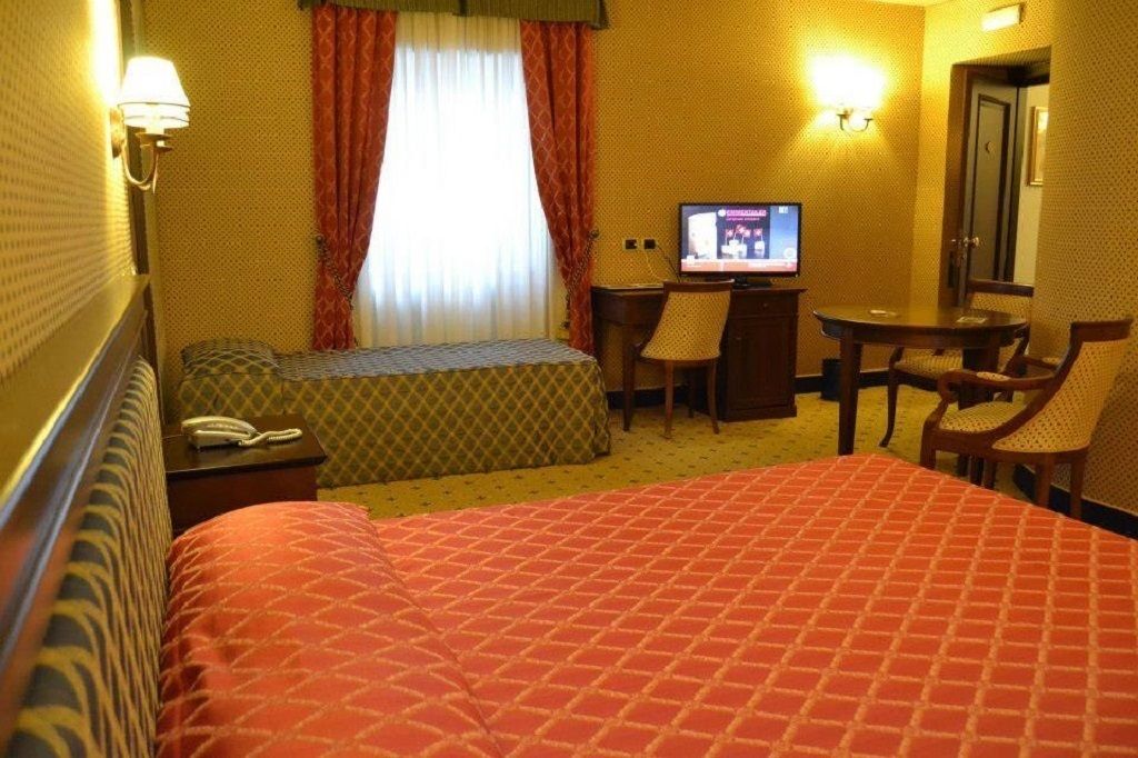 Ein Hotelzimmer mit einem großen Bett, einem Schreibtisch mit Stuhl, einem Fernseher und einem Telefon.
