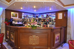 Una zona de bar con mostrador de madera, taburetes y una variedad de botellas y vasos.