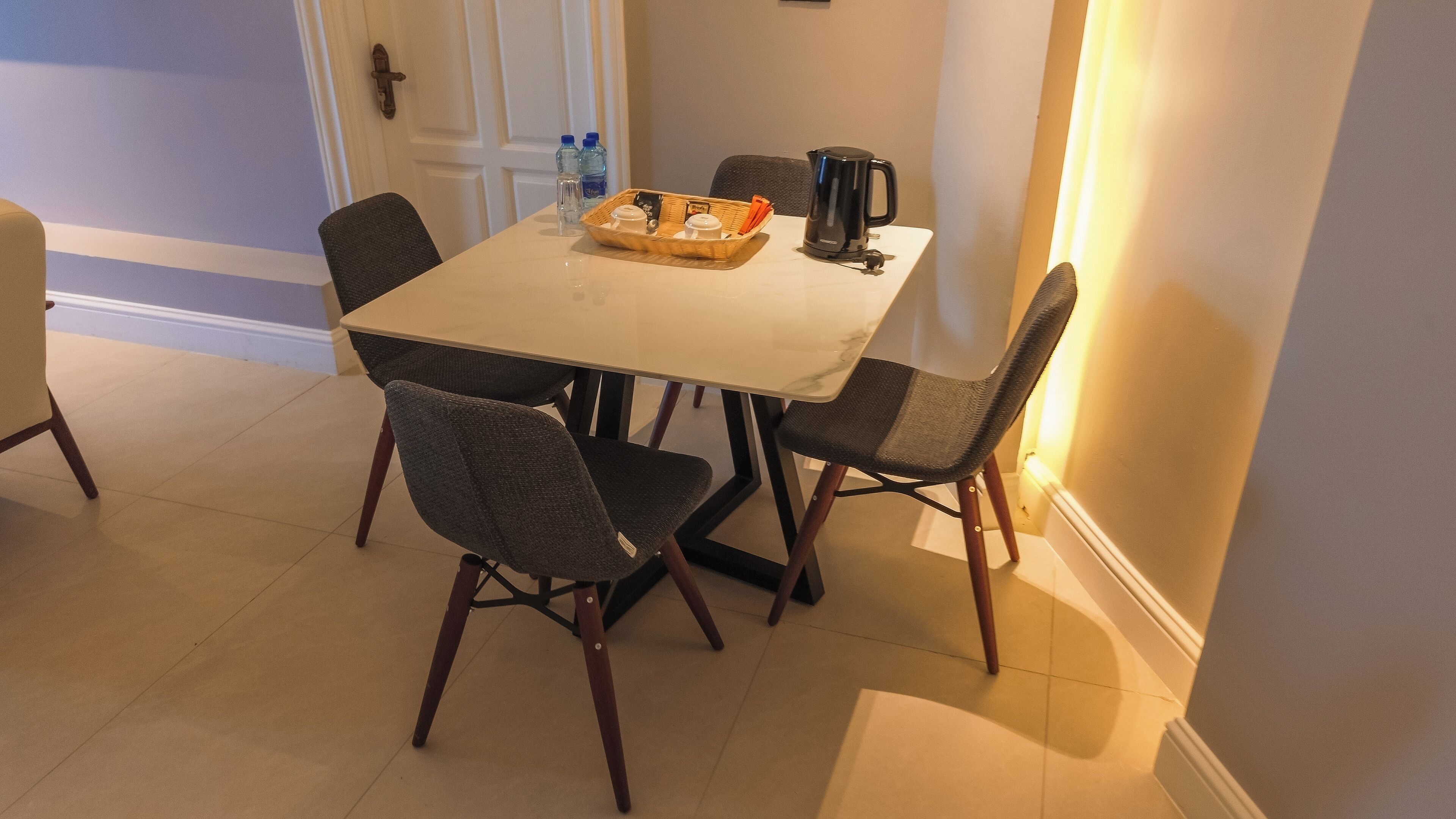 A dining area with a white table, four chairs, a coffee maker, and a tray with condiments.